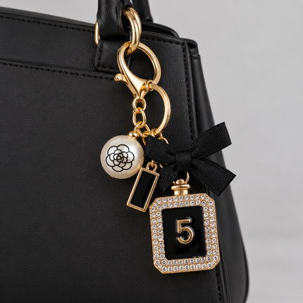  Portachiavi accessorio dorato con cristalli, fiocco nero e pendenti applicato a una borsa nera, immagine illustrativa