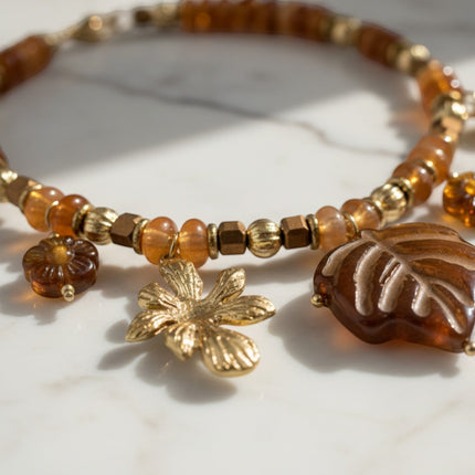 Tempo A Tempo boho chic necklace featuring amber-colored beads and gold-tone flower and leaf charms on marble surface