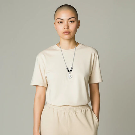 Modella indossa collana uomo Tempo A Tempo 2Jewels in acciaio con ciondolo ancora e perle nere su t-shirt beige