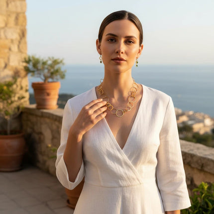 Tempo A Tempo gold necklace with interlocking circles worn by a woman in a white dress on a sunny terrace