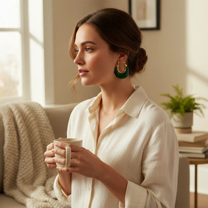 Tempo A Tempo Shelly gold-tone steel hoop earrings with green resin worn by a woman in a bright living room