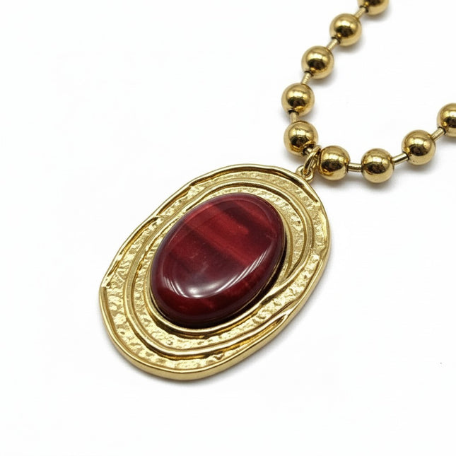 Tempo A Tempo gold-tone stainless steel necklace with ball chain and oval pendant featuring a red resin stone and hammered gold frame.