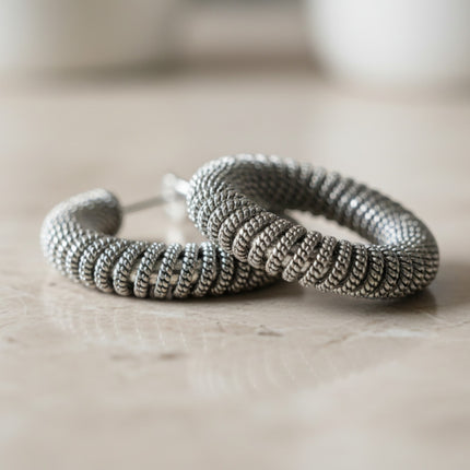 Orecchini a cerchio Tempo A Tempo in acciaio argentato con design a spirale intrecciata e finitura testurizzata.