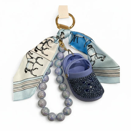 Portachiavi Tempo A Tempo con mini Crocs lilla, cristalli, foulard in raso stampa cavalli e perle opalescenti.