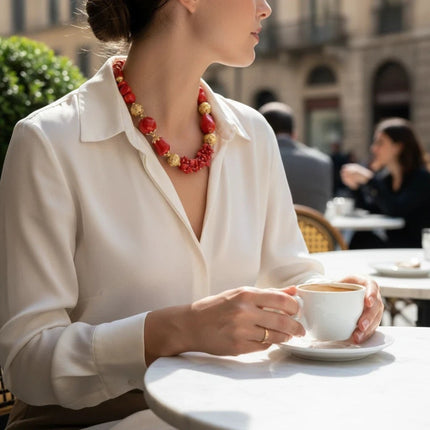 Tempo A Tempo statement necklace with red coral-effect beads and gold spheres worn by a woman at an outdoor cafe.